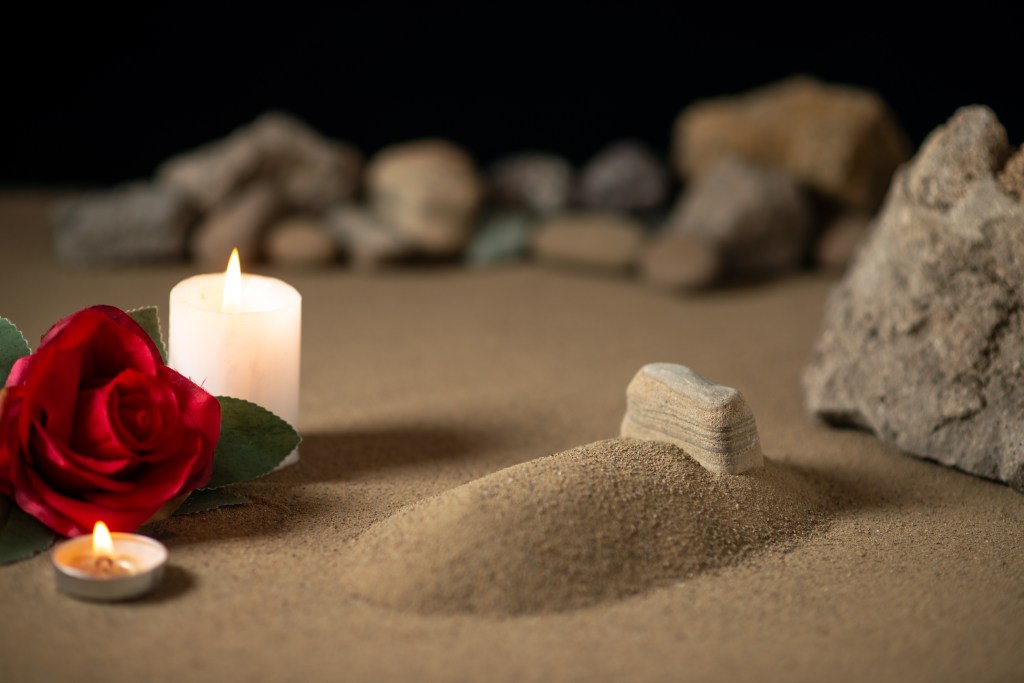 "Little grave with candle and stones on sand funeral war moon" by "mdjaff" from Freepik.com